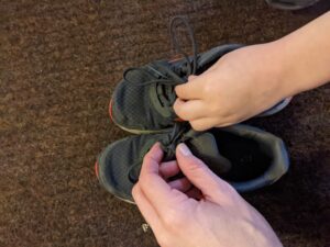 The picture shows the bloggers son trying to tie a shoe knot